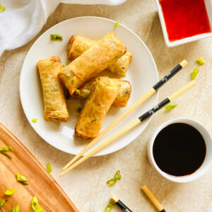 air fryer frozen spring rolls on a plate with chopsticks and soy sauce and thai chili sauce