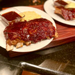 air fryer reheated ribs on a plate with a side of barbeque sauce and polenta