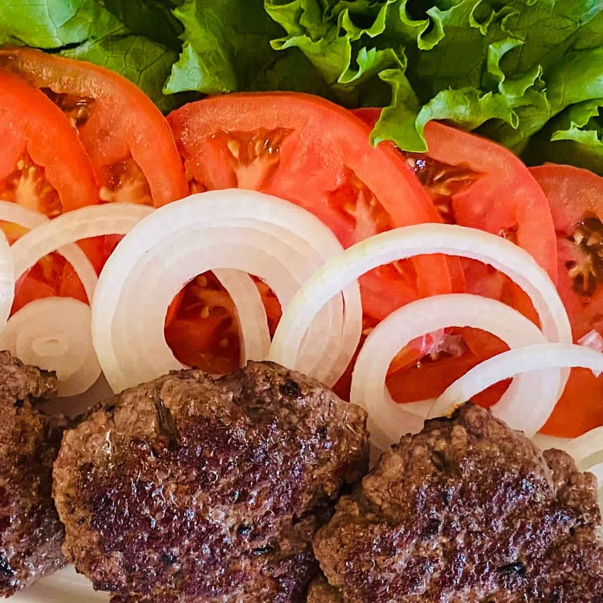 reheated burger in air fryer next to lettuce, tomato and onions sliced