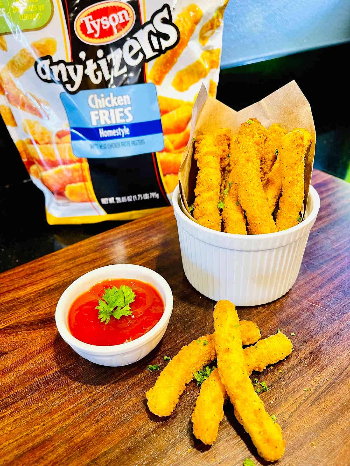 air fryer chicken fries in a bowl next to marinara sauce with a bag of tyson any'tizers chicken fries in the background