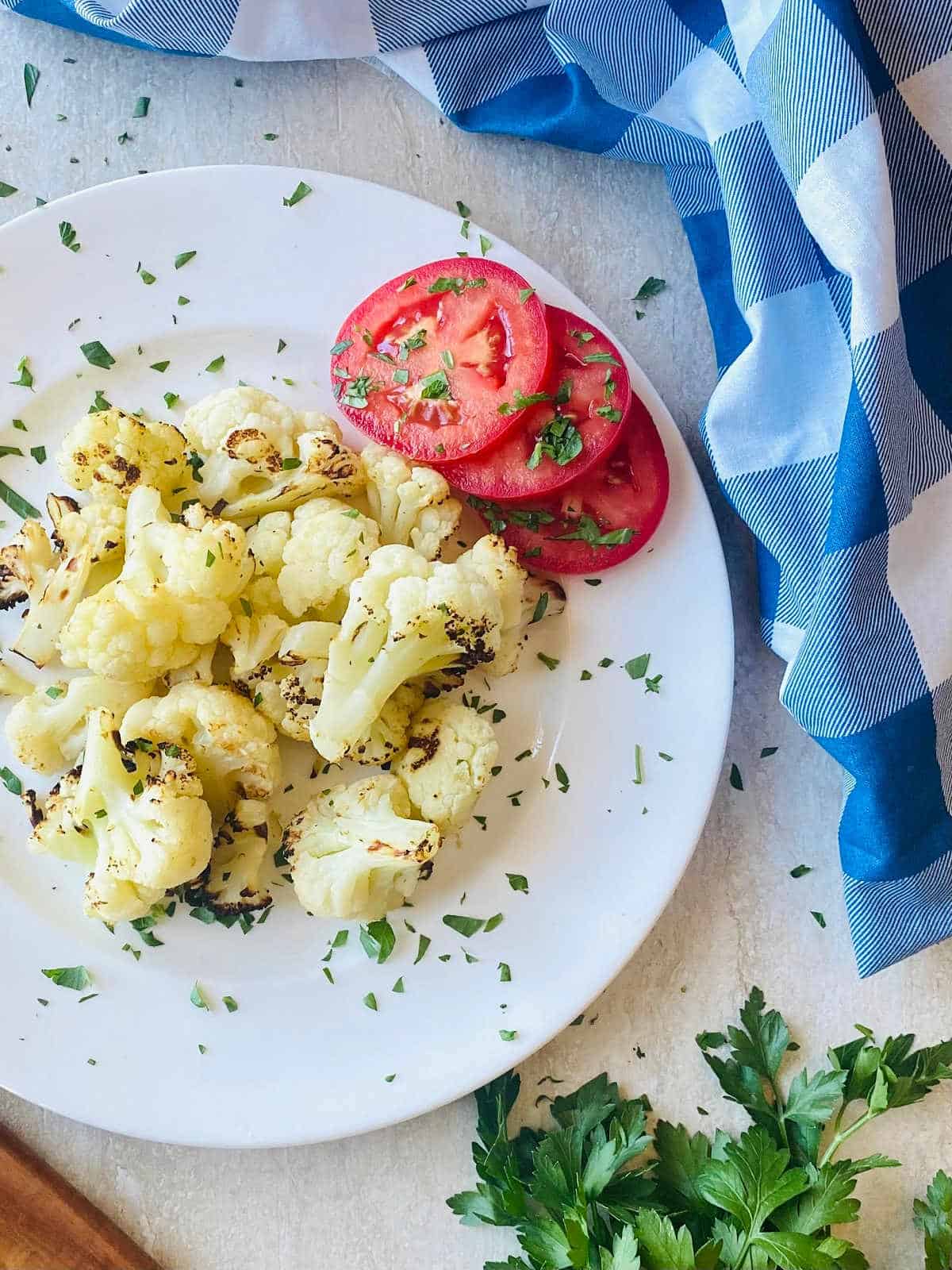air fryer frozen cauliflower on a plate next to tomatoes and parsley