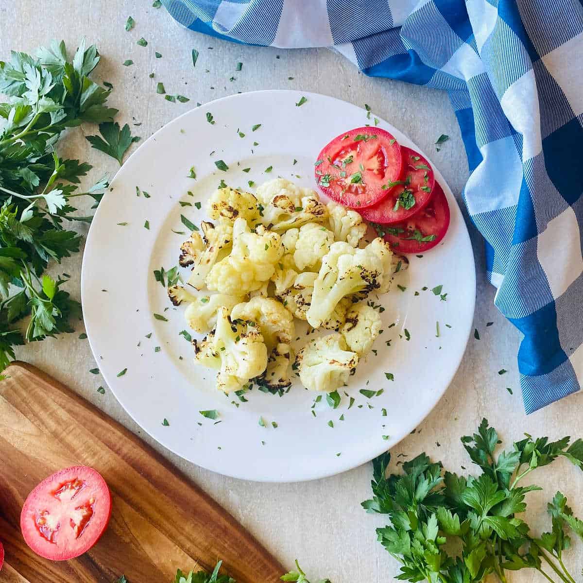 frozen cauliflower air fryer on a plate next to tomato and parsley