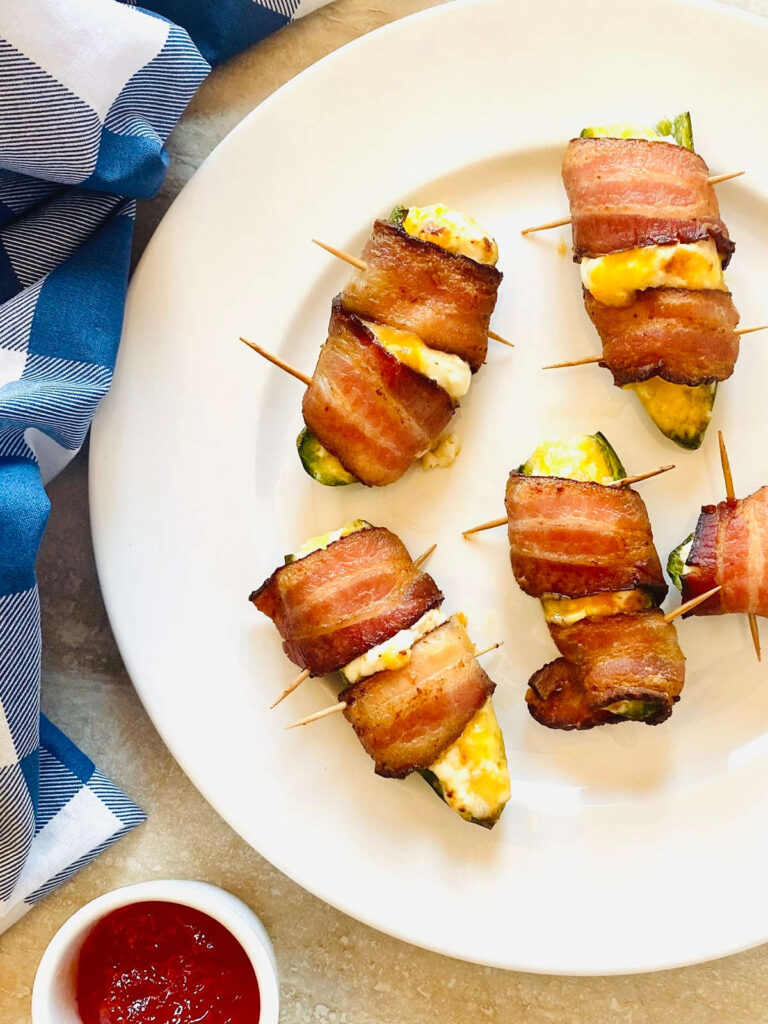 air fryer bacon wrapped jalapeno poppers on a plate next to a side of raspberry chipotle dipping sauce