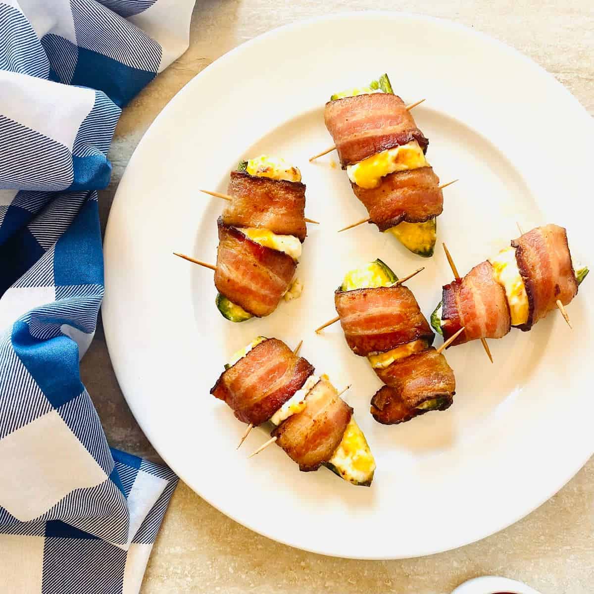 air fryer bacon wrapped jalapeno poppers on a plate next to a blue napkin