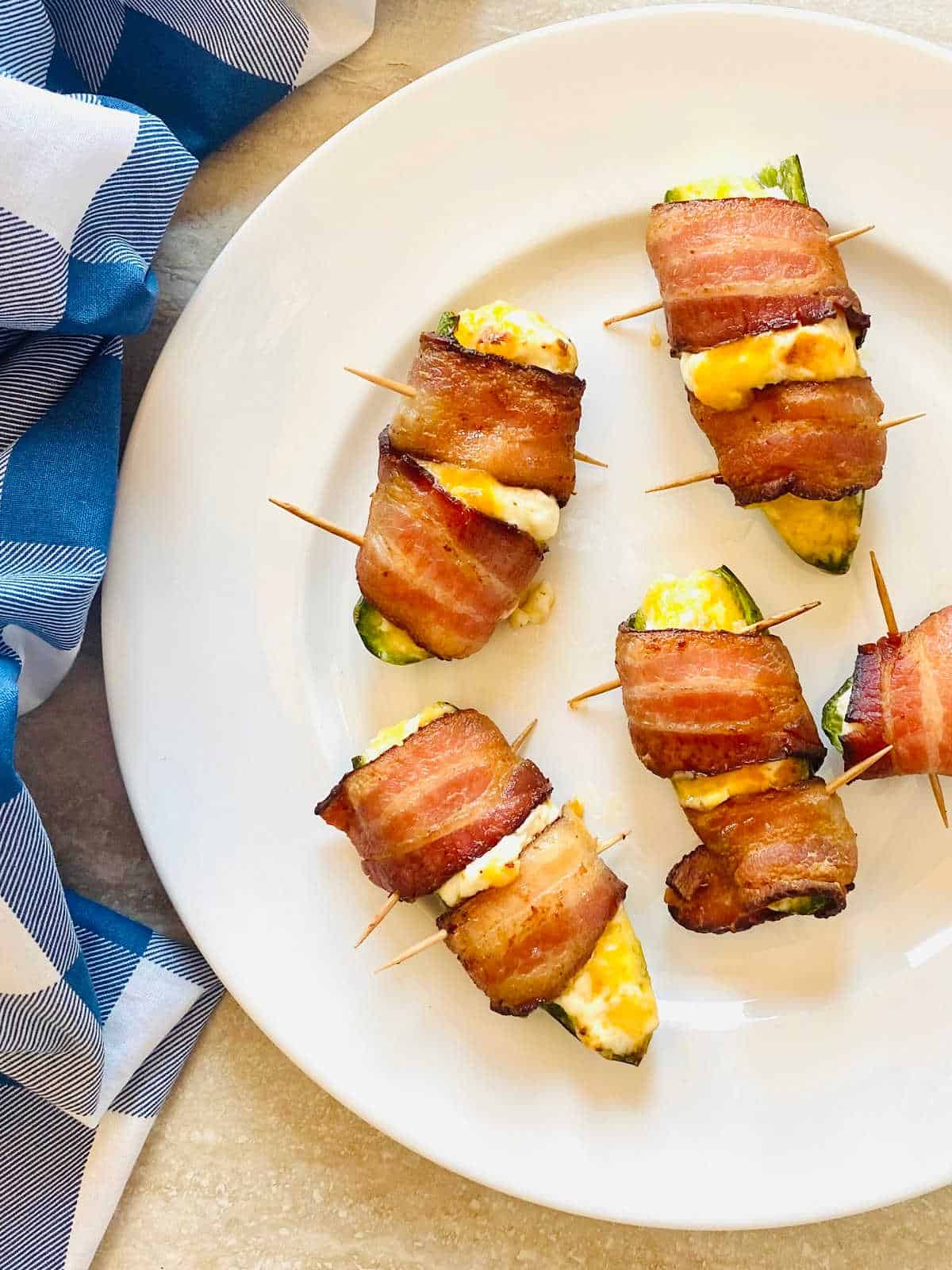 air fryer bacon wrapped stuffed jalapeno peppers on a plate next to a blue napkin